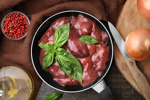 Raw chicken liver with basil in frying pan and products on wooden table, flat lay photo