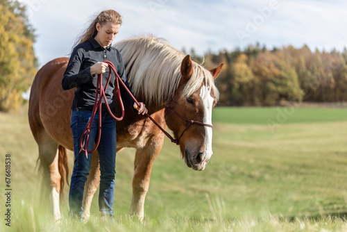 A young woman and her noriker coldblood draught horse on a meadow in autumn outdoors