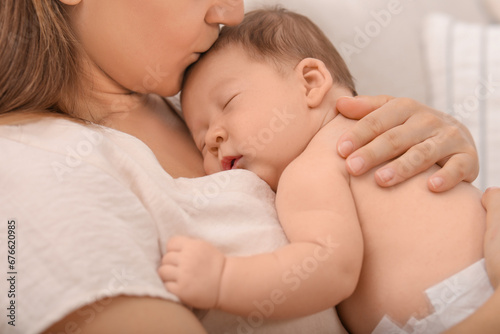 Mother kissing her cute newborn baby indoors