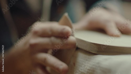 Hands of artisan polishing wooden board with sand paper, sawdust flying around in the air. Close-up shot