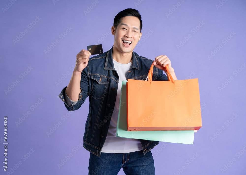 Image of asian man using phone and shopping bag on purple background Image of asian man using phone and shopping bag on purple background
