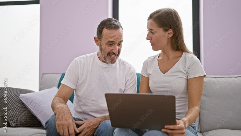 Casual lifestyle at home, confident father and lovely daughter enjoying fun internet time on laptop, sitting relaxed on sofa, expressing positive smiles and hugging each other warmly.