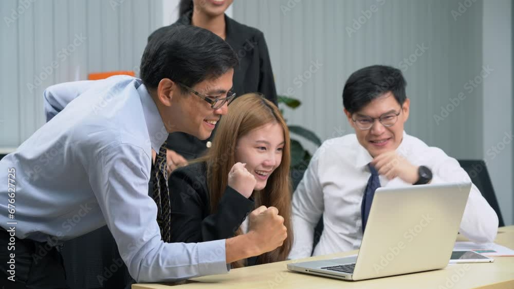 Group of happy asian business people sitting on a table raised fists cheering at laptop celebrating achievement goals to success in meeting at office Group of happy asian business people sitting on a table raised fists cheering at laptop celebrating achievement goals to success in meeting at office