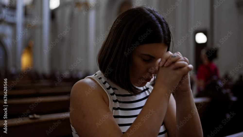 Young beautiful hispanic woman praying on a church bench at Augustinian Church in Vienna
