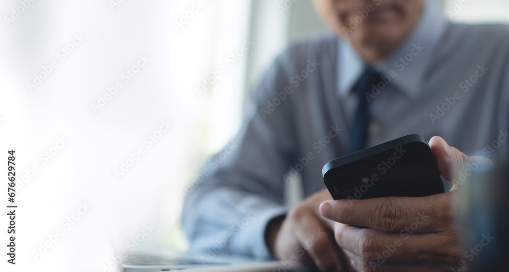 Close up of businessman using mobile smart phone during working on laptop computer at office. Asian business man hand holding smartphone, connecting the internet, online working Close up of businessman using mobile smart phone during working on laptop computer at office. Asian business man hand holding smartphone, connecting the internet, online working