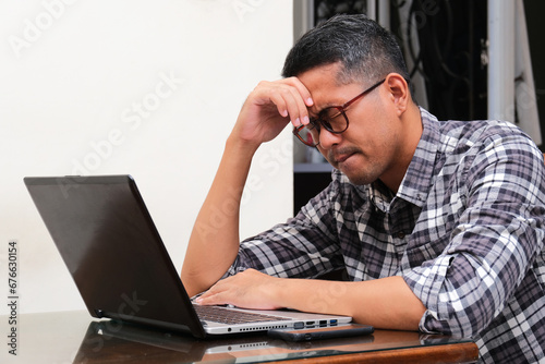 Adult Asian man sitting in front of laptop with stress expression photo