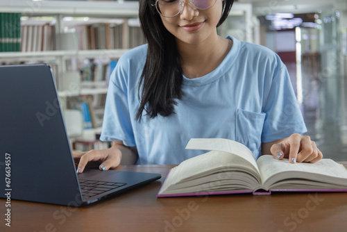 Female university student study in the school library.She using laptop and learning online, writing , sitting, laptop, book