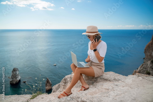 Freelance women sea working on the computer. Good looking middle aged woman typing on a laptop keyboard outdoors with a beautiful sea view. The concept of remote work. © svetograph