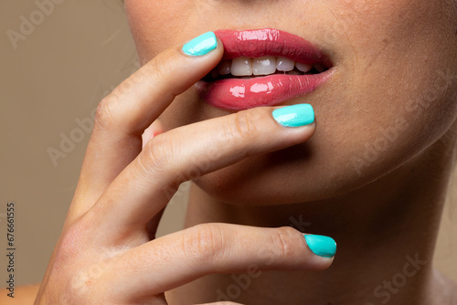 Caucasian woman wearing natural makeup and blue nail polish on beige background