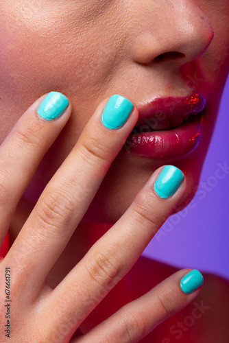 Close up of caucasian woman wearing pink lipstick and blue nail polish on purple background