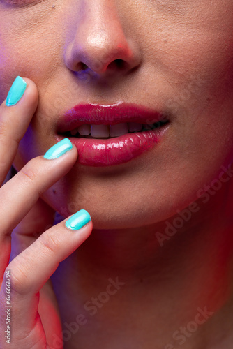 Close up of caucasian woman wearing pink lipstick and blue nail polish on purple background