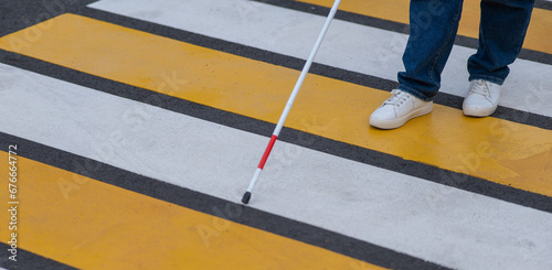 Close-up of the legs of a blind woman crossing the road at a crosswalk with a cane. 