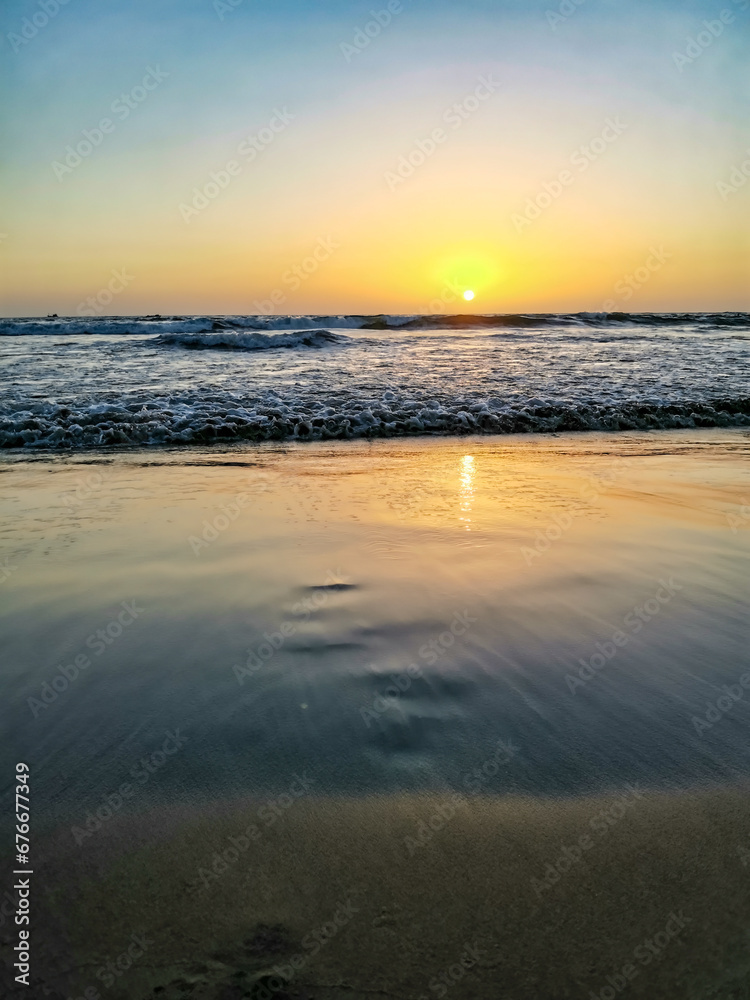 Sunset on Mandrem Beach in Goa, India. Bright and colorful sunset over the Indian Ocean, the Arabian Sea. A tropical beach with yellow sand and a bronze sunset.