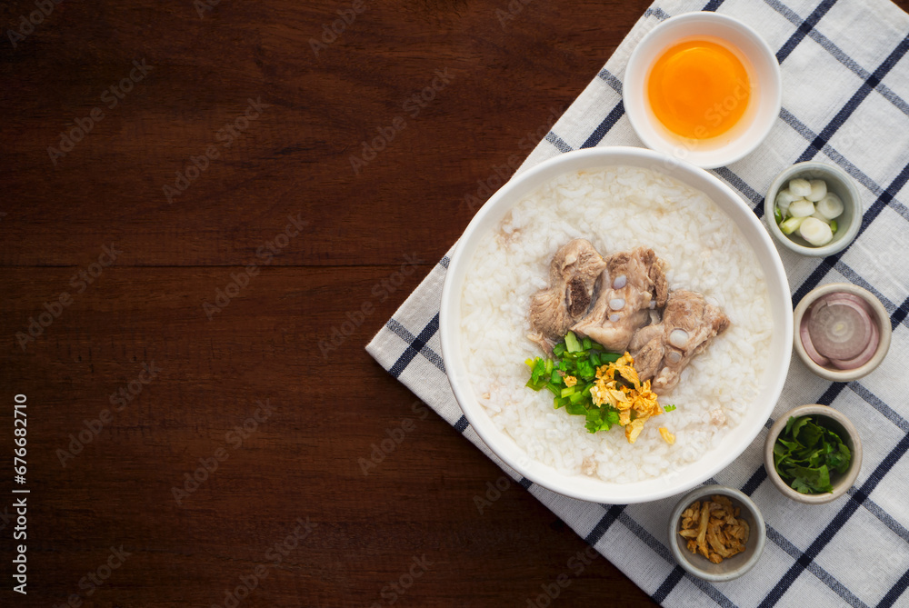 Top view of rice soup or boiled rice with pork ribs in bowl on wooden table background. Thai Food