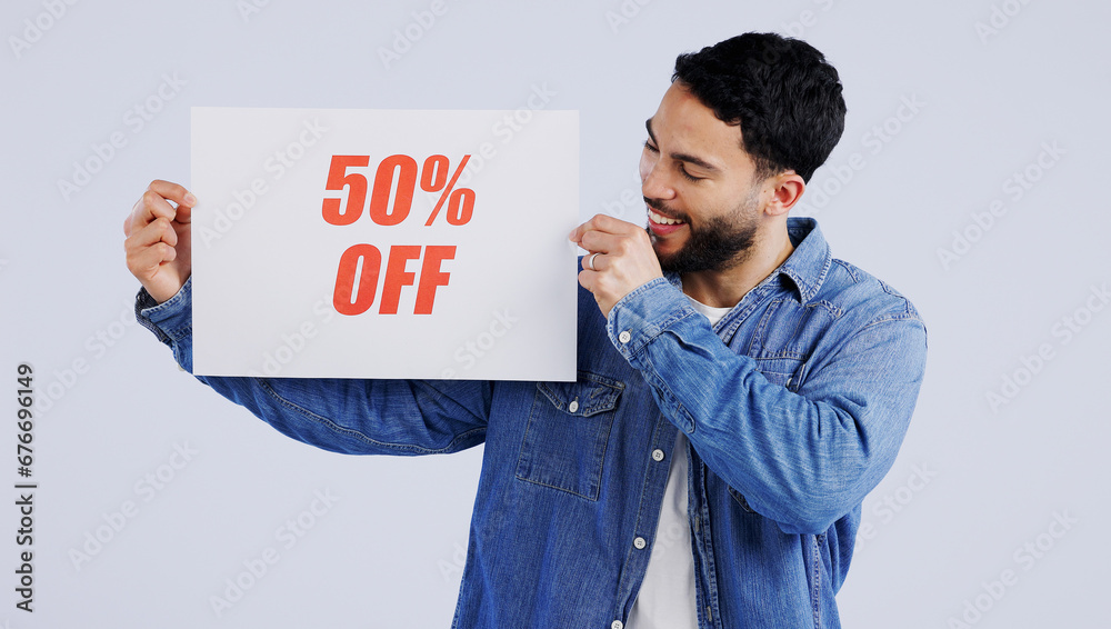 Happy man, sign and sale in discount, promotion or banner against a gray studio background. Male person or model smile with billboard, poster or half price in advertising or marketing for store promo Happy man, sign and sale in discount, promotion or banner against a gray studio background. Male person or model smile with billboard, poster or half price in advertising or marketing for store promo