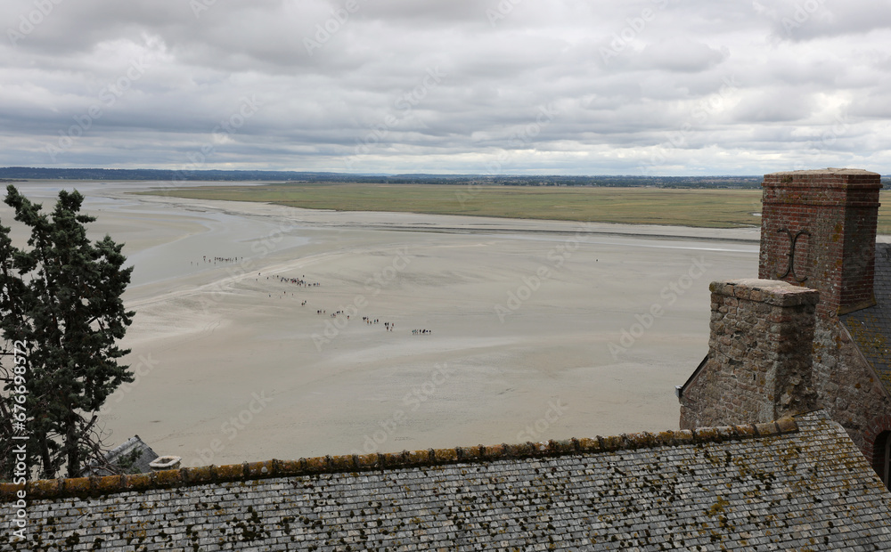 view from Mont Saint Michel Abbey in Normandy in Northern France and little people walking on the sand at low tide