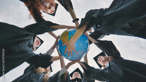 Fotografie Graduating students embrace a geographical globe of the world