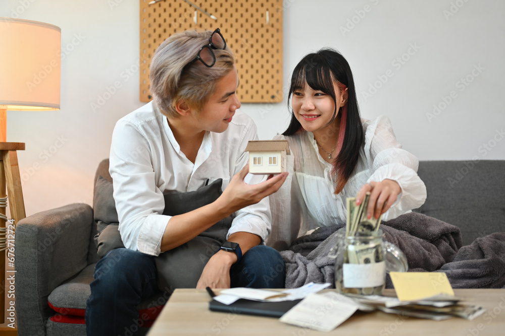Happy young couple putting money into savings jars, planning to buy their future new house Happy young couple putting money into savings jars, planning to buy their future new house