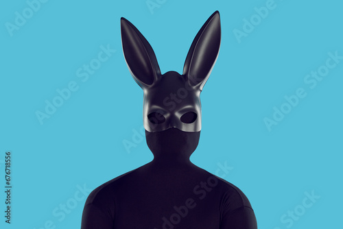 Studio shot of man disguised in black rabbit costume. Male model in faceless skintight monochromatic bodysuit and kinky long eared bunny mask standing like black silhouette isolated on blue background photo
