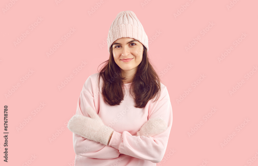 Studio portrait of happy beautiful young woman in warm winter clothes. Pretty Caucasian lady in pastel pink hat, cozy sweatshirt and mittens standing on light pink background. Winter fashion concept Studio portrait of happy beautiful young woman in warm winter clothes. Pretty Caucasian lady in pastel pink hat, cozy sweatshirt and mittens standing on light pink background. Winter fashion concept