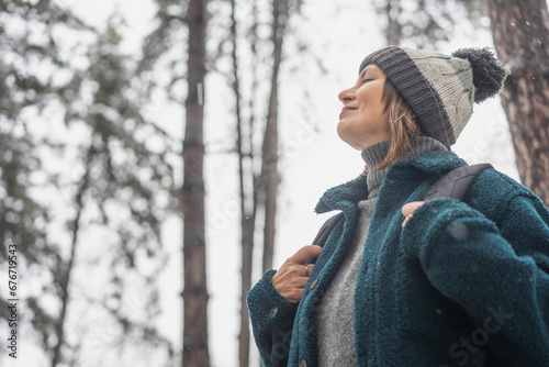 A young mature woman breathes fresh air and enjoys the snowfall in the winter forest. Winter walks and activity concept