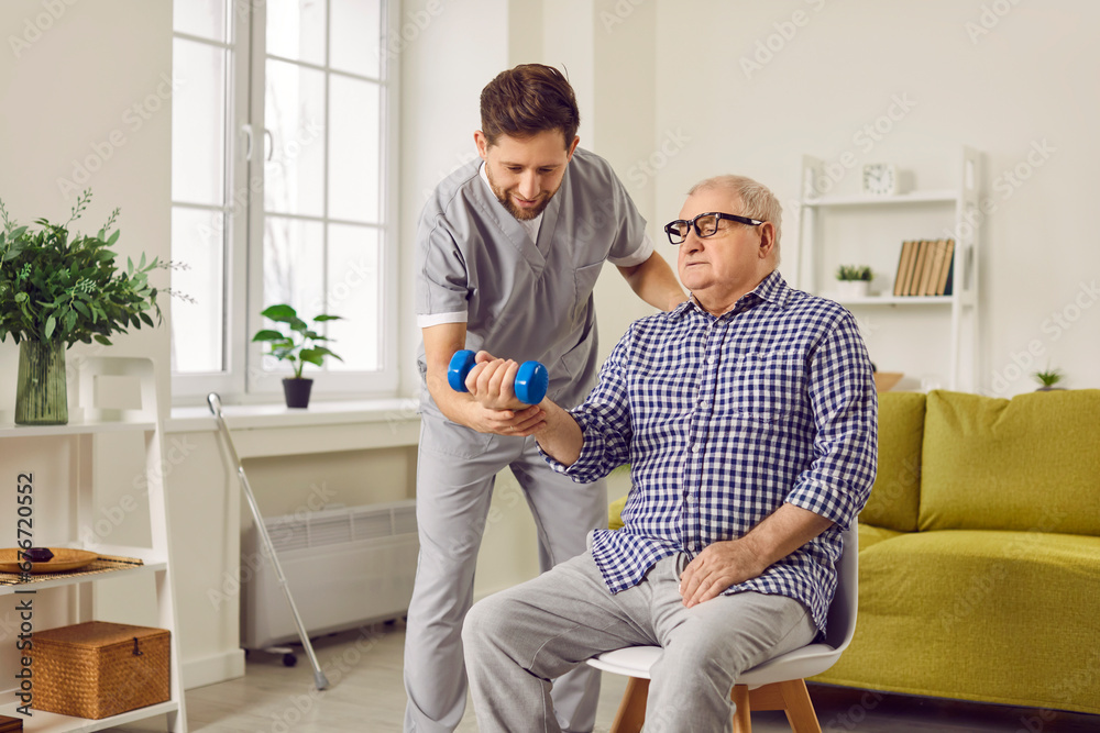 Senior man doing exercise using dumbbells with support from nurse.Young smiling caregiver physiotherapist helping elderly man in lifting dumbell at retirement. Recovery and nursering home concept. Senior man doing exercise using dumbbells with support from nurse.Young smiling caregiver physiotherapist helping elderly man in lifting dumbell at retirement. Recovery and nursering home concept.
