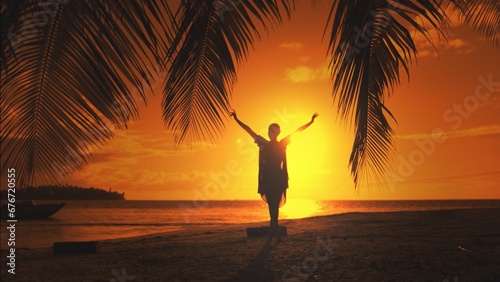 Woman silhouette against orange sunset sky. Young slim woman walking tropical island beach under the coconut palm tree branch. Relaxing, travel, tourism, exotic holiday vacation.