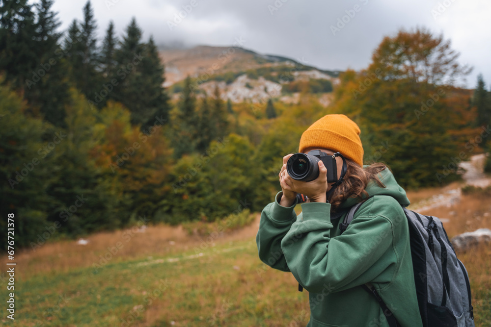 Woman traveler photographer taking photo using camera during autumn trip to mountains