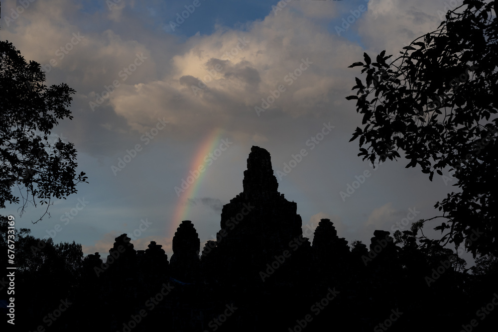 Fototapeta premium As the sun sets. Bayon temple, Siem Reap, Cambodia in the late evening light. A rainbow is visible in the sky.