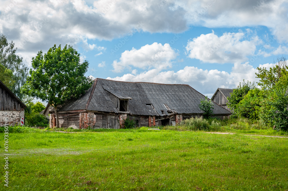 View on abandoned farm. Rural Latvian landscape with field, buildings, blue sky and clouds in sunny day. View on abandoned farm. Rural Latvian landscape with field, buildings, blue sky and clouds in sunny day.