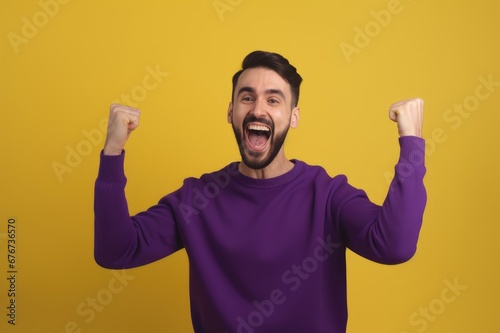 A young bearded man standing against a yellow background rejoicing in success and victory, clenching his fists in joy and happy to achieve his goal and tasks. Positive emotions. generative AI