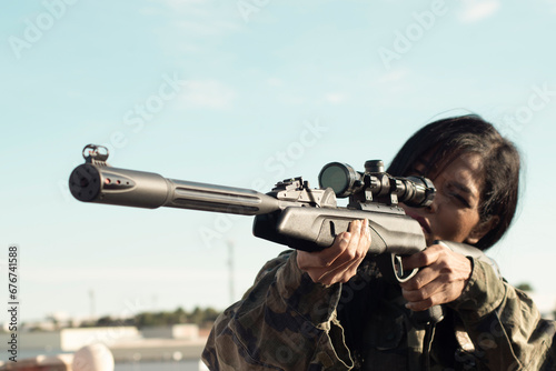 A female sniper with dark skin in camouflage military clothing holds a gun, takes aim, selective focus, optical sight close-up. Concept of military operations with the participation of female soldiers photo