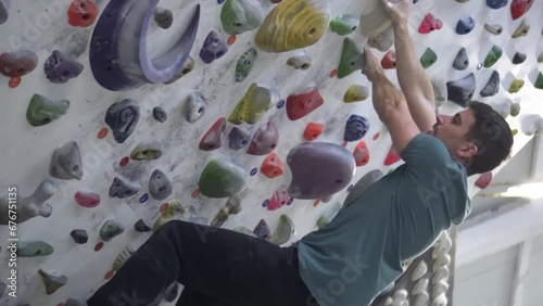 Side shot of a man climbing on an artificial climbing wall inside a climbing gym. Sporting activity and healthy living.
