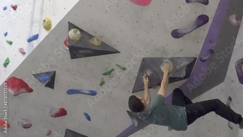 Young man bouldering in an indoor climbing gym across a large overhang of high difficulty. Active life and sport