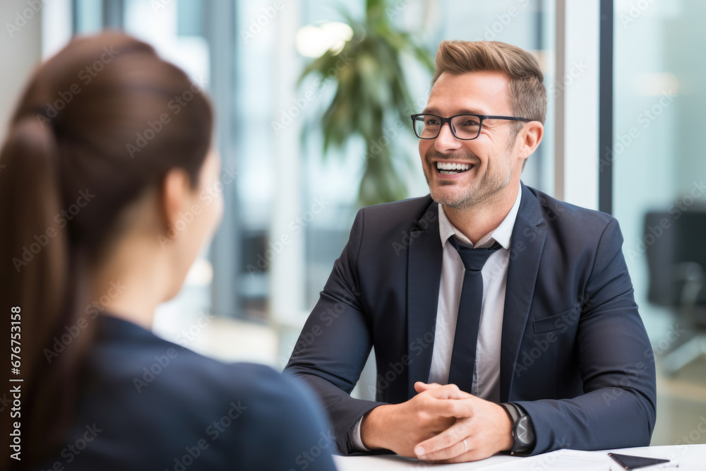 A male businessperson laughing as he meets with a woman at a job interview. A male businessperson laughing as he meets with a woman at a job interview.