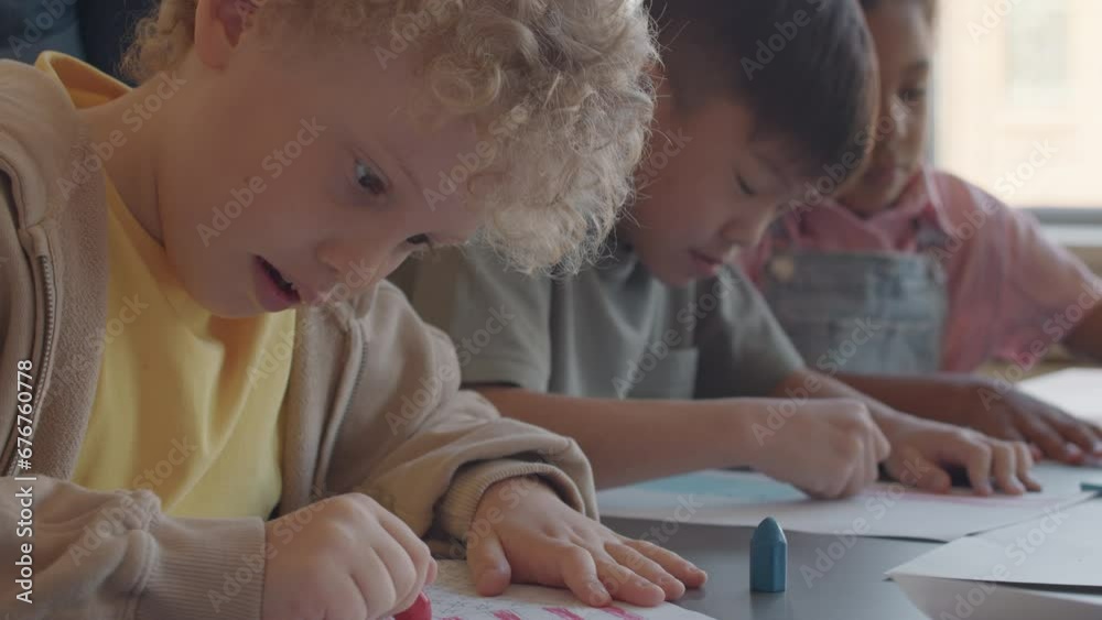 Tilt down shot of curly haired blond schoolboy sitting at desk and drawing American flag with crayon on paper during art class in elementary school Tilt down shot of curly haired blond schoolboy sitting at desk and drawing American flag with crayon on paper during art class in elementary school