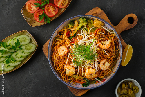 Image of a plate of noodles with shrimp pieces and side dishes on a black background