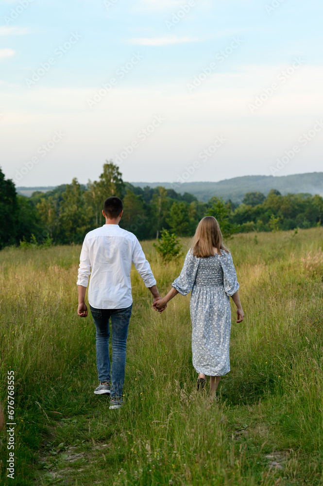 A boy and a girl are holding hands and walking in an open field