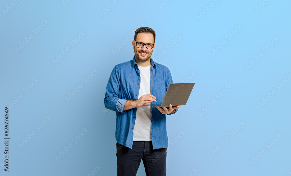 Portrait of confident businessman doing online research over laptop against blue background Portrait of confident businessman doing online research over laptop against blue background