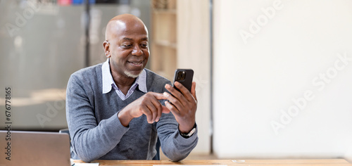 Happy african american businessman using phone mobile at workplace texting sms, smiling black man looking at smartphone browsing internet. photo