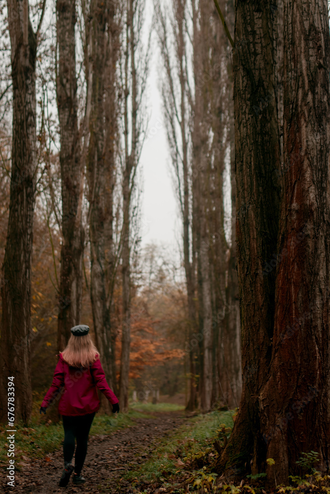 Beautiful young relaxed woman in black cap and burgundy jacket and walking through trees on an autumn day in forest Beautiful young relaxed woman in black cap and burgundy jacket and walking through trees on an autumn day in forest
