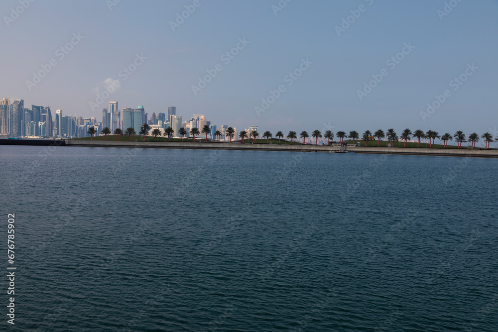A view of the garden of the Museum of Islamic Art in Qatar, with the sea, boats and palm trees, with the Doha Towers as a background A view of the garden of the Museum of Islamic Art in Qatar, with the sea, boats and palm trees, with the Doha Towers as a background