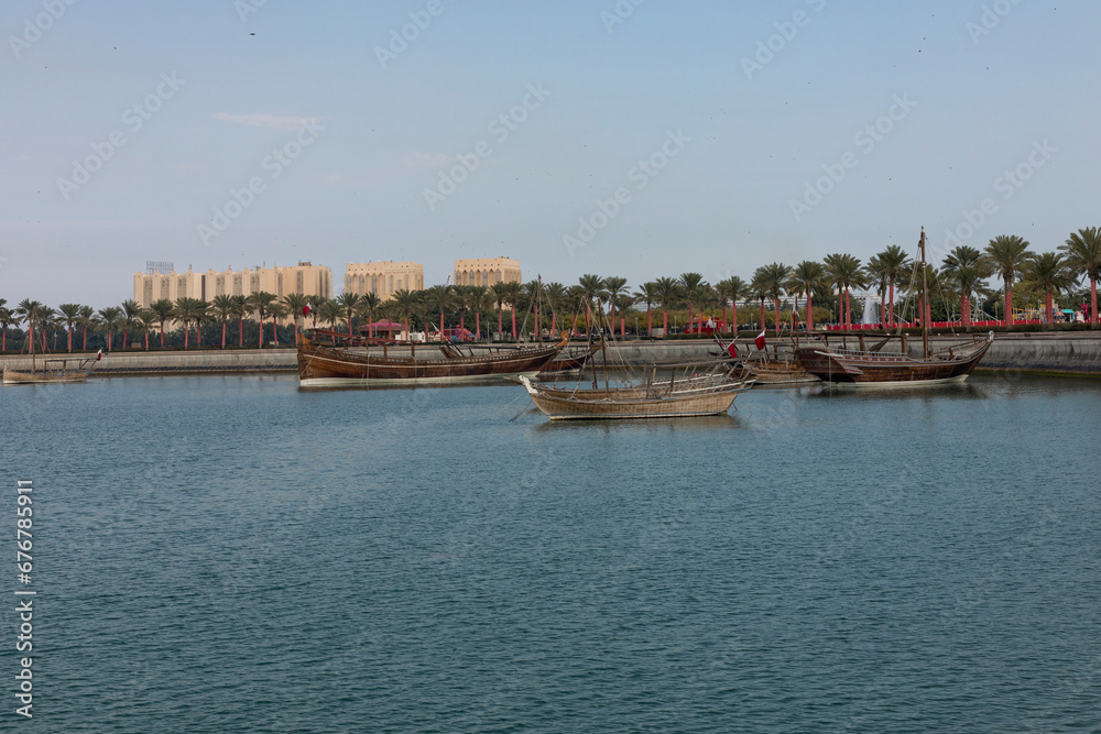 A view of the garden of the Museum of Islamic Art in Qatar, with the sea, boats and palm trees, with the Doha Towers as a background