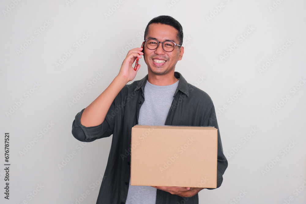 Adult Asian man smiling when calling and holding a package box Adult Asian man smiling when calling and holding a package box