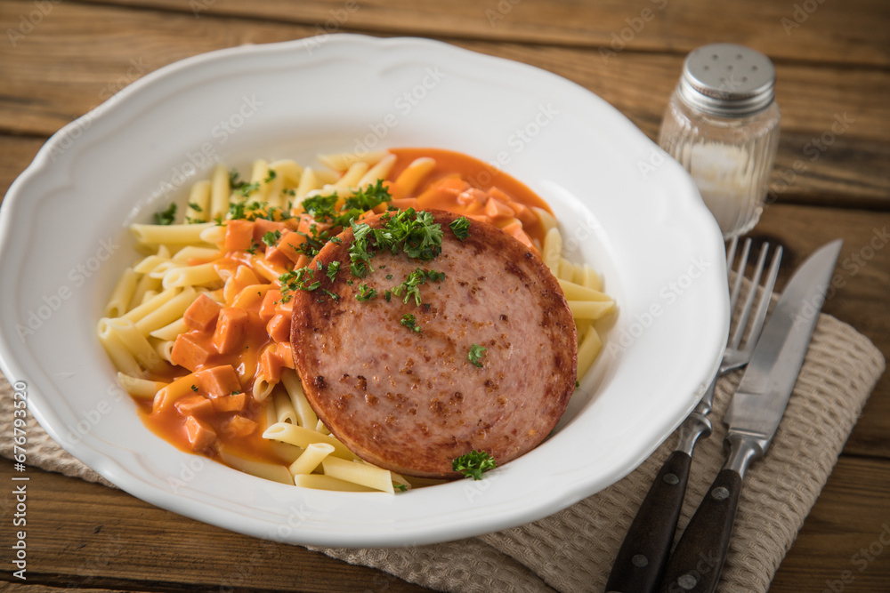 Jägerschnitzel nach DDR GDR Rezept mit Jagdwurst gebraten, Makkaroni Penne Nudeln, Tomatensoße, Petersilie mit Porzellan tiefer Teller, Besteck, Salzstreuer, Serviette, rustikal dunkel Holz Hintergund Jägerschnitzel nach DDR GDR Rezept mit Jagdwurst gebraten, Makkaroni Penne Nudeln, Tomatensoße, Petersilie mit Porzellan tiefer Teller, Besteck, Salzstreuer, Serviette, rustikal dunkel Holz Hintergund