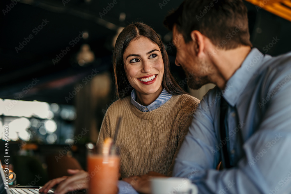 Side view of cheerful couple using a laptop together while sitting in a cafe Side view of cheerful couple using a laptop together while sitting in a cafe