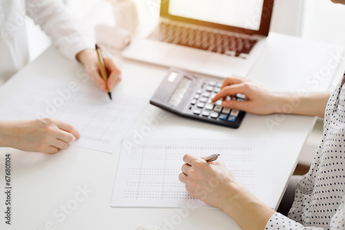 Two accountants using a calculator and laptop computer for counting taxes at white desk in office. Teamwork in business audit and finance