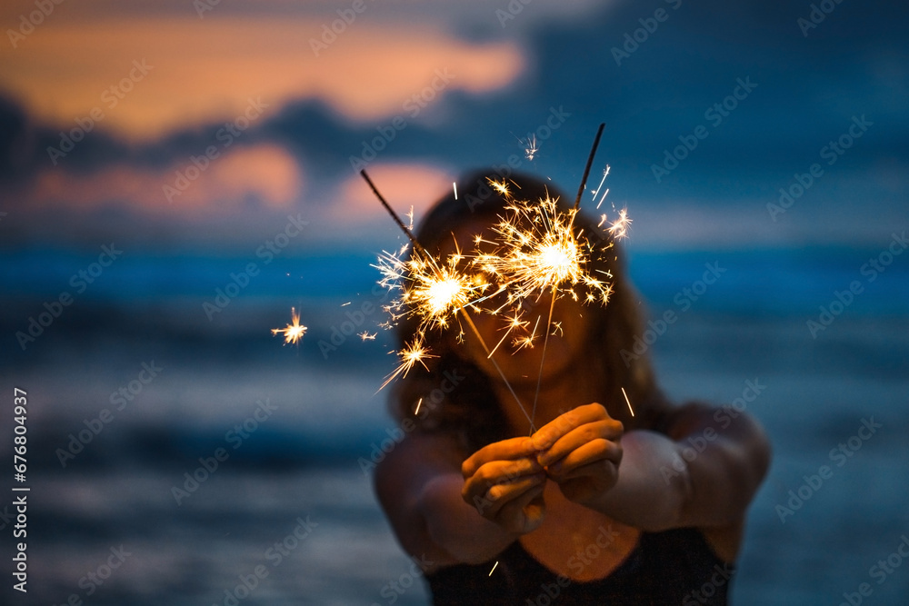 Young woman holding sparkler celebrating new years eve on the beach - obrazy, fototapety, plakaty 
