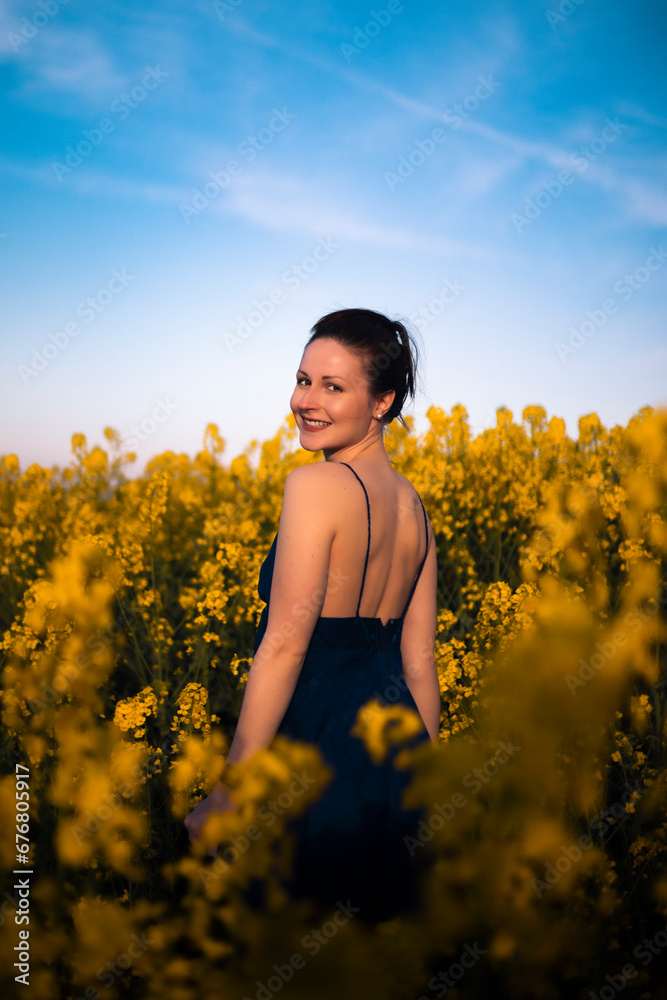 Fototapeta premium schöne Frau mit blauem Sommerkleid in einem Rapsfeld