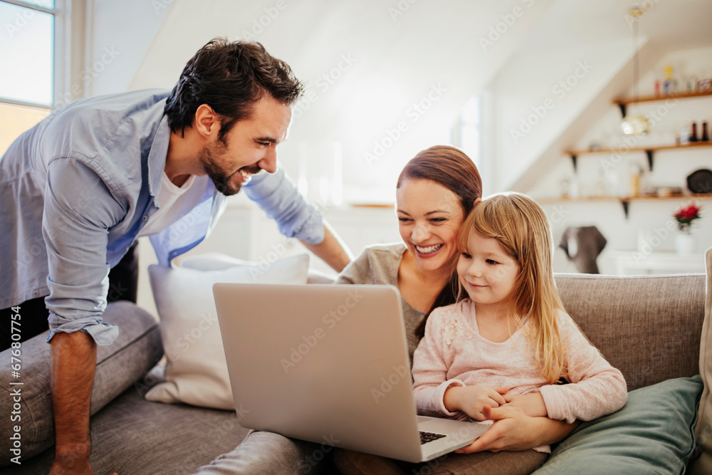 Happy family with little daughter having fun with laptop at home